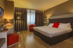 Una habitación de hotel con una cama grande, un escritorio con lámpara, una silla roja y un televisor.