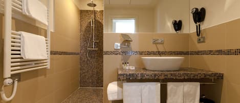 A modern bathroom with a shower, a sink, and a toilet. There are towels hanging on a rack and a phone on the wall.