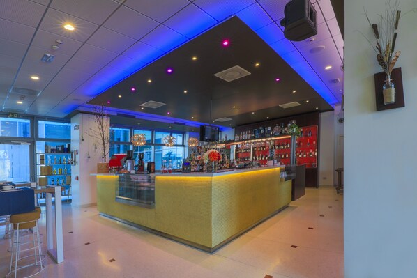 Zona de bar moderna con una barra central, estanterías con botellas y un área de asientos con taburetes.