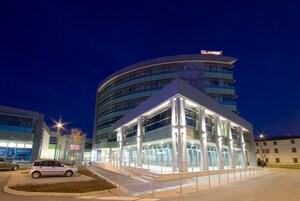 Un hotel moderno con fachada de vidrio, un área de estacionamiento y un edificio con el rótulo 'GLAMOUR'.