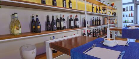 Interior de restaurante con botellas de vino en estanterías, una mesa de comedor con mantel azul y una vela sobre la mesa.