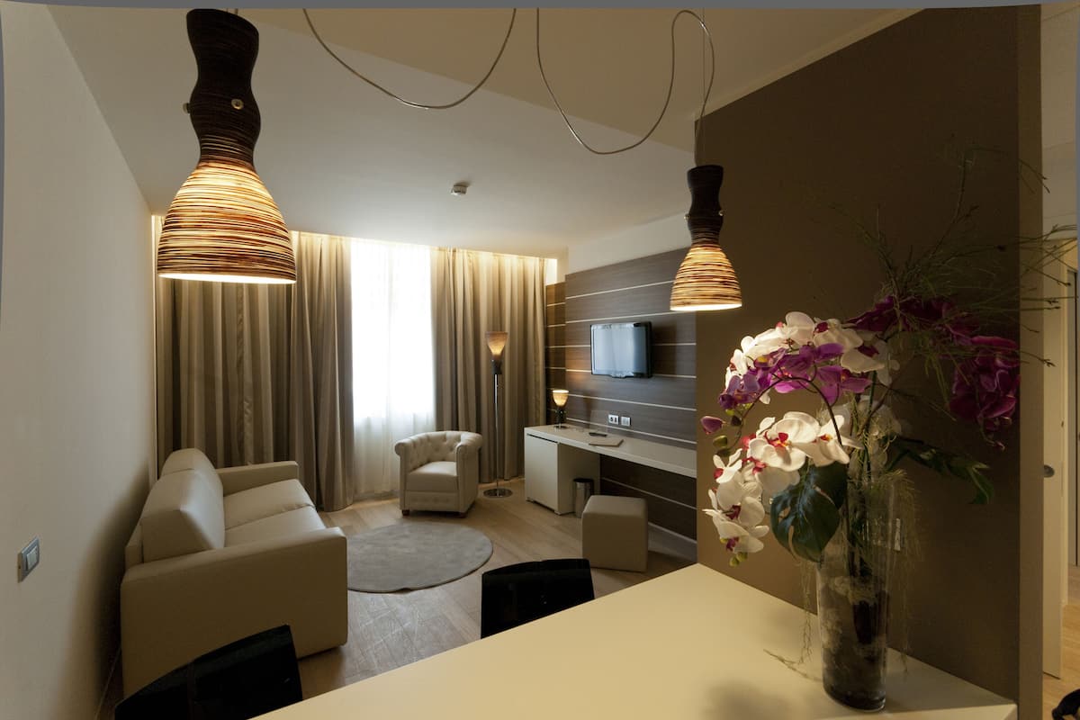 Una sala de estar moderna con un sofá, una mesa de comedor y un televisor. Hay un florero con flores sobre la mesa.