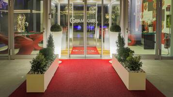 L’entrée d’un hôtel, avec un tapis rouge, des portes en verre et une enseigne indiquant « Hôtel GEAMOUR ».