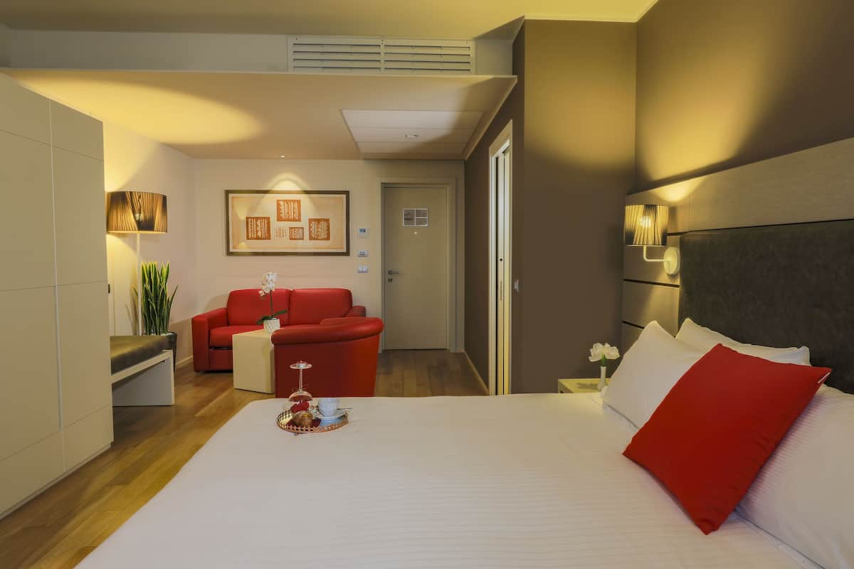 Habitación de hotel con cama, un sofá rojo, una mesita con bandeja y un cuadro en la pared.
