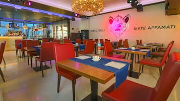 Un restaurante con sillas rojas, mesas de madera, una zona de bar y una pared con un mural de un tigre y el nombre "SIATE AFFAMATI".
