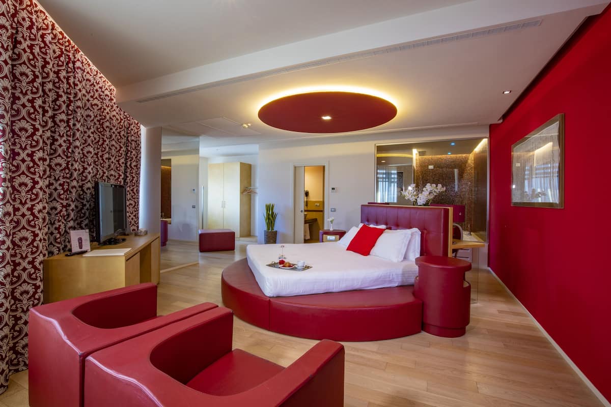 Una habitación de hotel moderna con una cama redonda, detalles en rojo, un televisor y una planta.