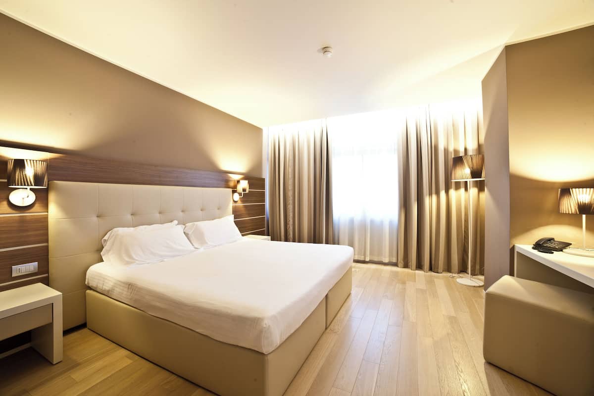 Habitación de hotel con una cama grande, lámparas de noche, un escritorio y una ventana con cortinas.