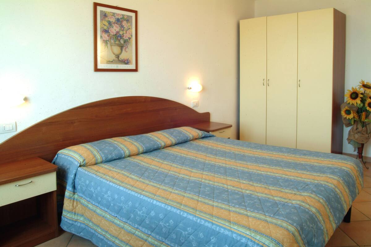 A bedroom with a wooden bed, a nightstand, a wardrobe, and a wall-mounted light fixture.