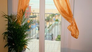 Un balcone con tende arancioni, una pianta in vaso e vista sulla spiaggia e sugli edifici.