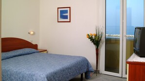 Una camera da letto con un letto, una televisione, un vaso con fiori e un quadro appeso al muro.