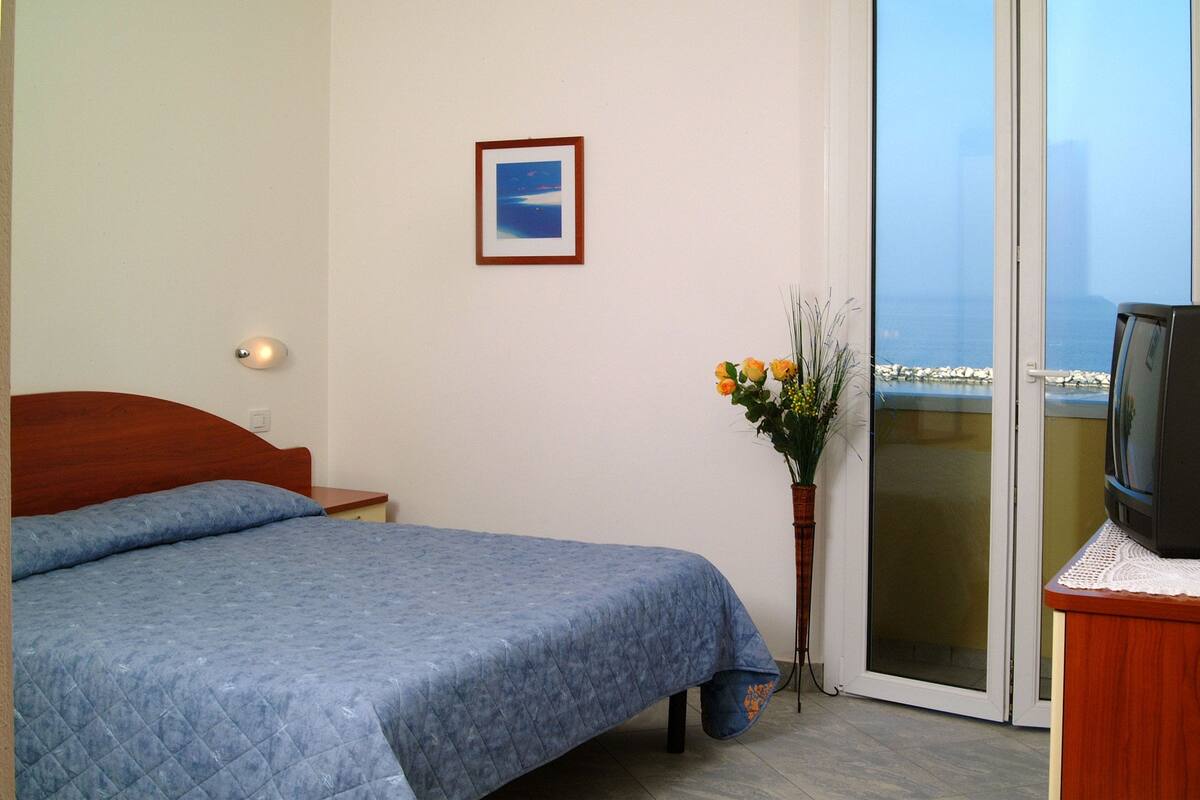 A bedroom with a bed, a television, a vase with flowers, and a picture on the wall.