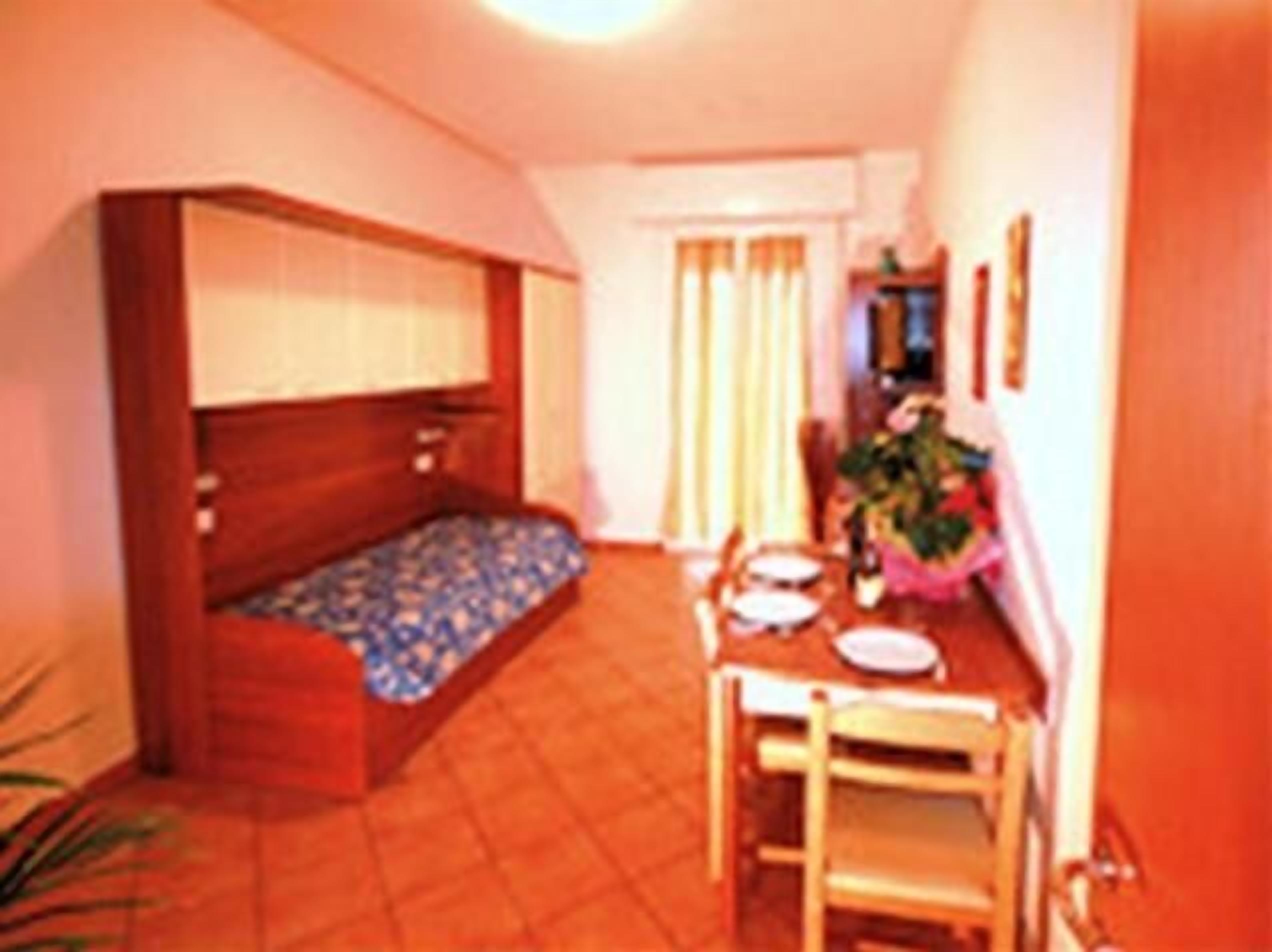 Una habitación pequeña y acogedora con cama, una mesa con sillas y una ventana con cortinas.