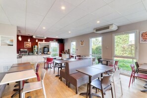 A restaurant with indoor seating, a kitchen area, and large windows.