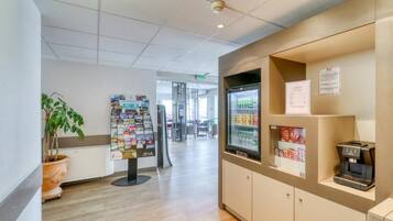 Zona de recepción con máquina de café, refrigerador con bebidas y un tablón de anuncios con varios avisos.