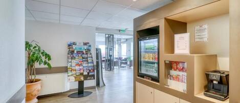 A reception area with a coffee machine, a refrigerator stocked with beverages, and a bulletin board with various notices.