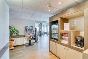A reception area with a coffee machine, a refrigerator stocked with beverages, and a bulletin board with various notices.