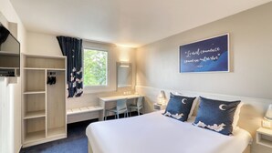 Habitación de hotel con cama, escritorio, silla, armario y ventana con cortinas.