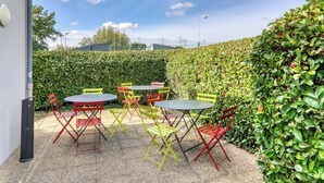 Un patio al aire libre con mesas y sillas, rodeado por un seto.