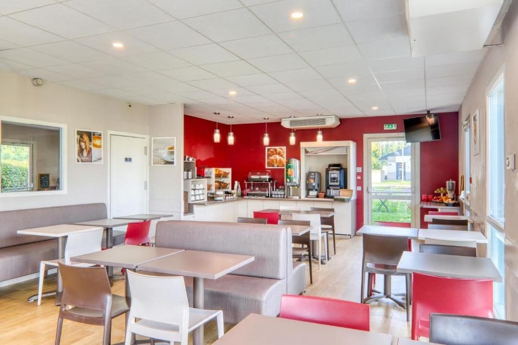 A modern cafe with multiple seating areas, including booths and tables, and a visible kitchen area.