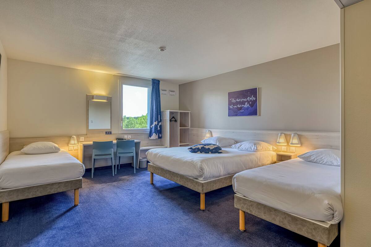 A hotel room with two beds, a desk, a chair, and a window with a view.