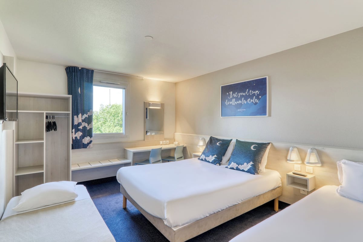 Une chambre d’hôtel comprenant un lit, des tables de chevet, un bureau, une armoire et une fenêtre avec des rideaux.