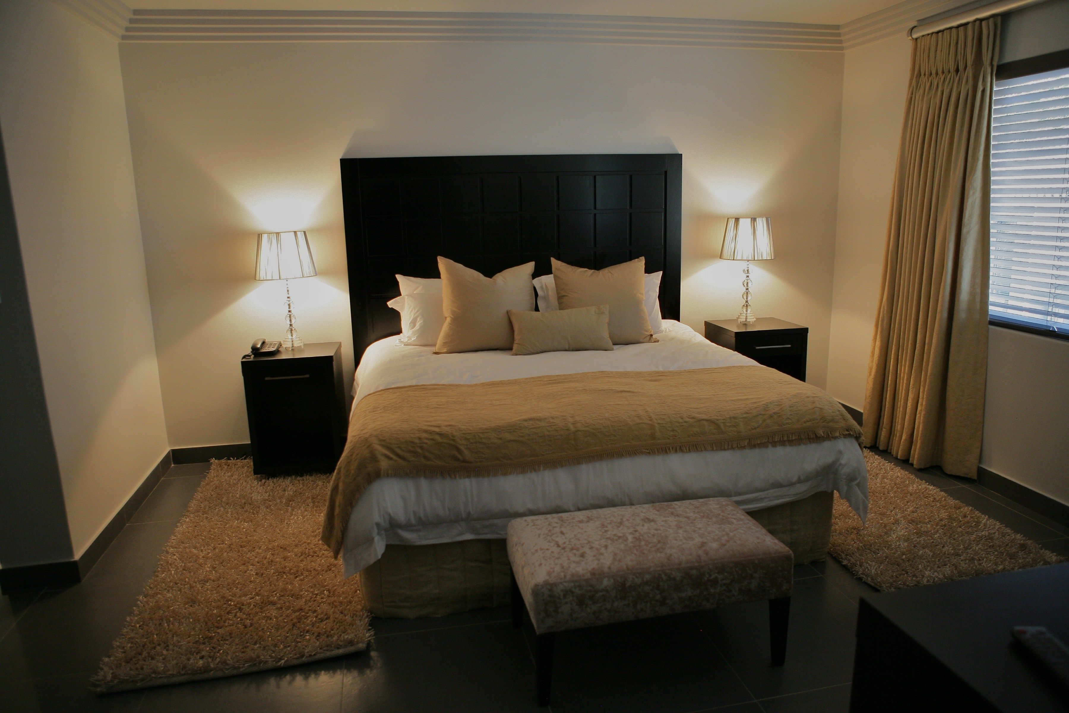 A neatly arranged bedroom with a large bed, two bedside tables with lamps, a bench, and a window with curtains.