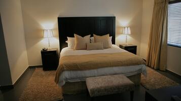 A neatly arranged bedroom with a large bed, two bedside tables with lamps, a bench, and a window with curtains.