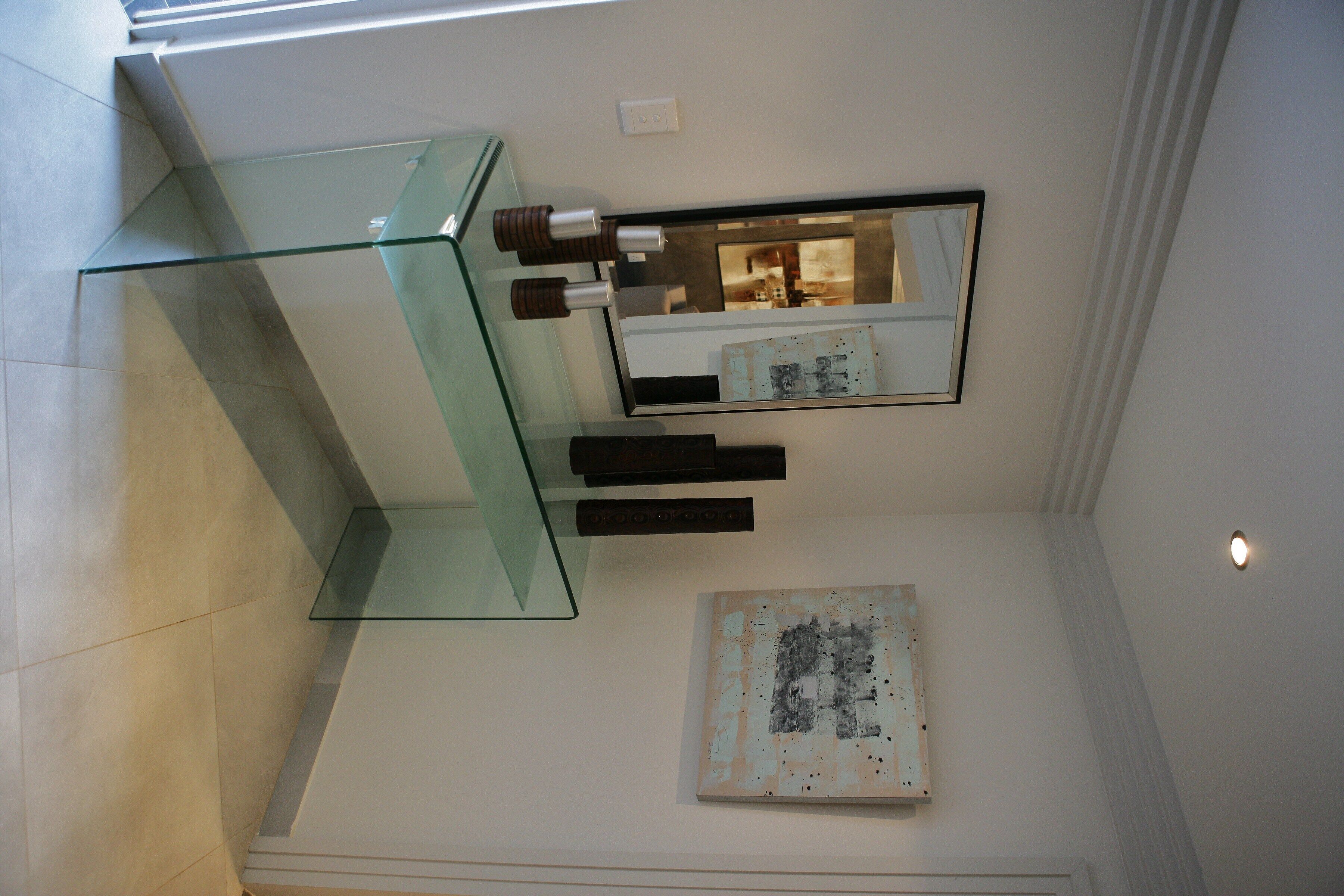 A modern bathroom with a glass shelf, a mirror, and a piece of abstract art on the wall.