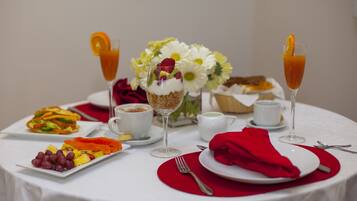 Une table dressée pour le petit-déjeuner, avec une variété de plats, notamment une assiette de fruits, un verre de jus d’orange et un verre de jus d’orange garni d’une tranche d’orange.
