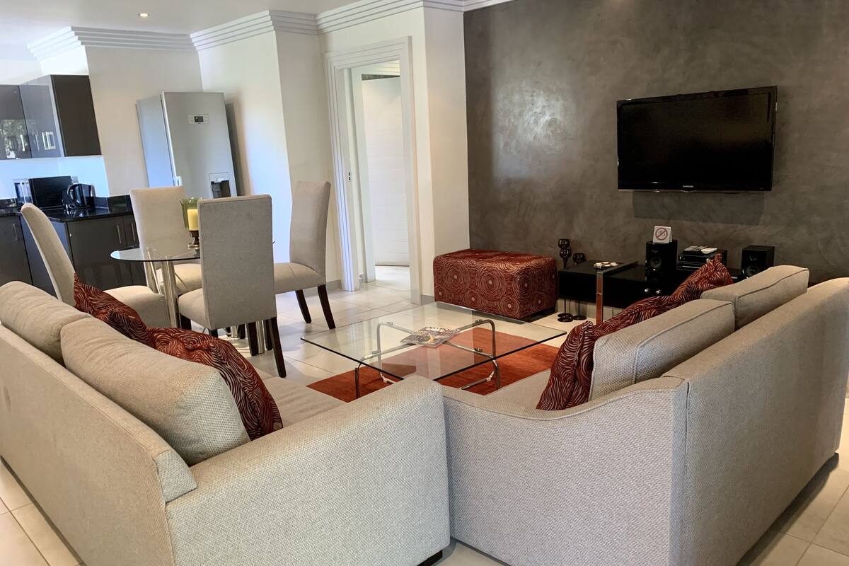 Un salon moderne avec un canapé d’angle, une table basse en verre et un téléviseur à écran plat fixé au mur.