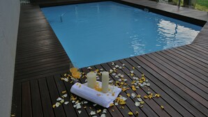 A swimming pool with a wooden deck, two candles, and scattered flower petals.