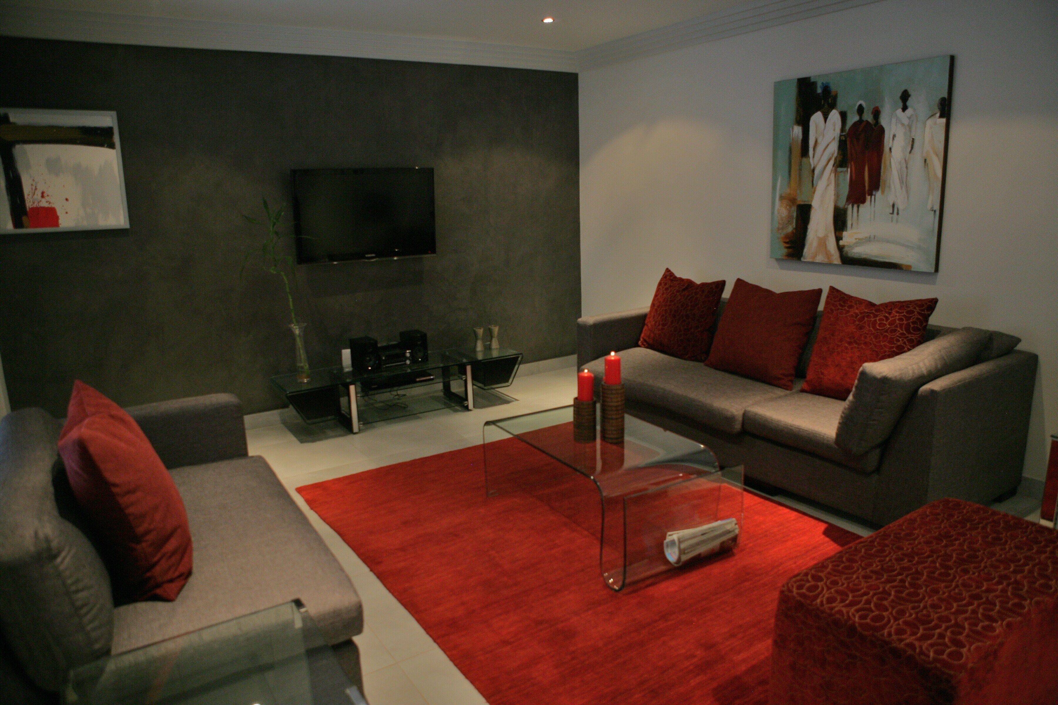 Un salon moderne avec un canapé gris, des coussins rouges, une table basse en verre et un téléviseur à écran plat fixé au mur.
