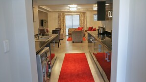 A modern kitchen with a red carpet, a sofa with red cushions, and a dining area with a table and chairs.