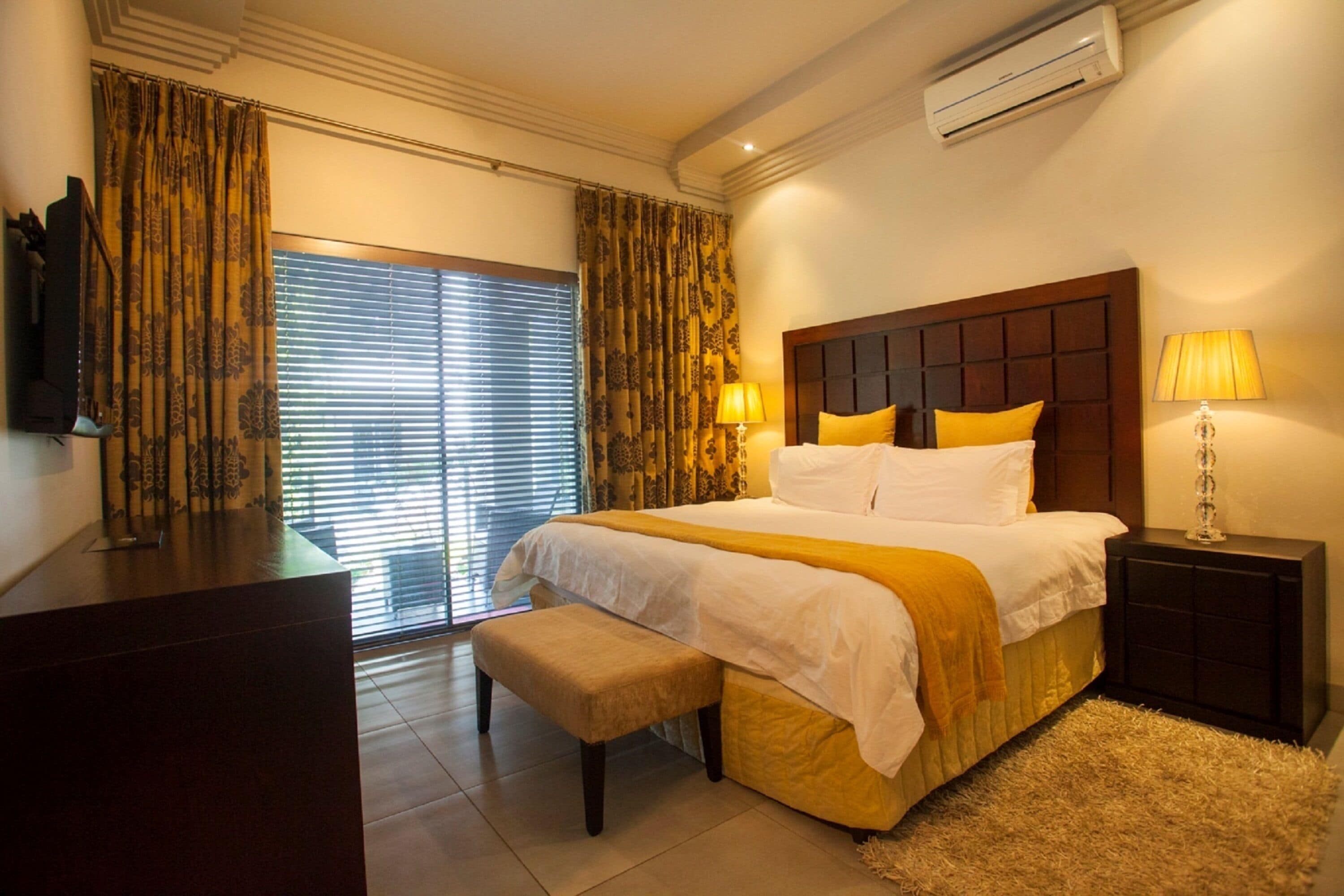 A hotel room with a large bed, a bench, a desk, a TV, and a window with curtains.