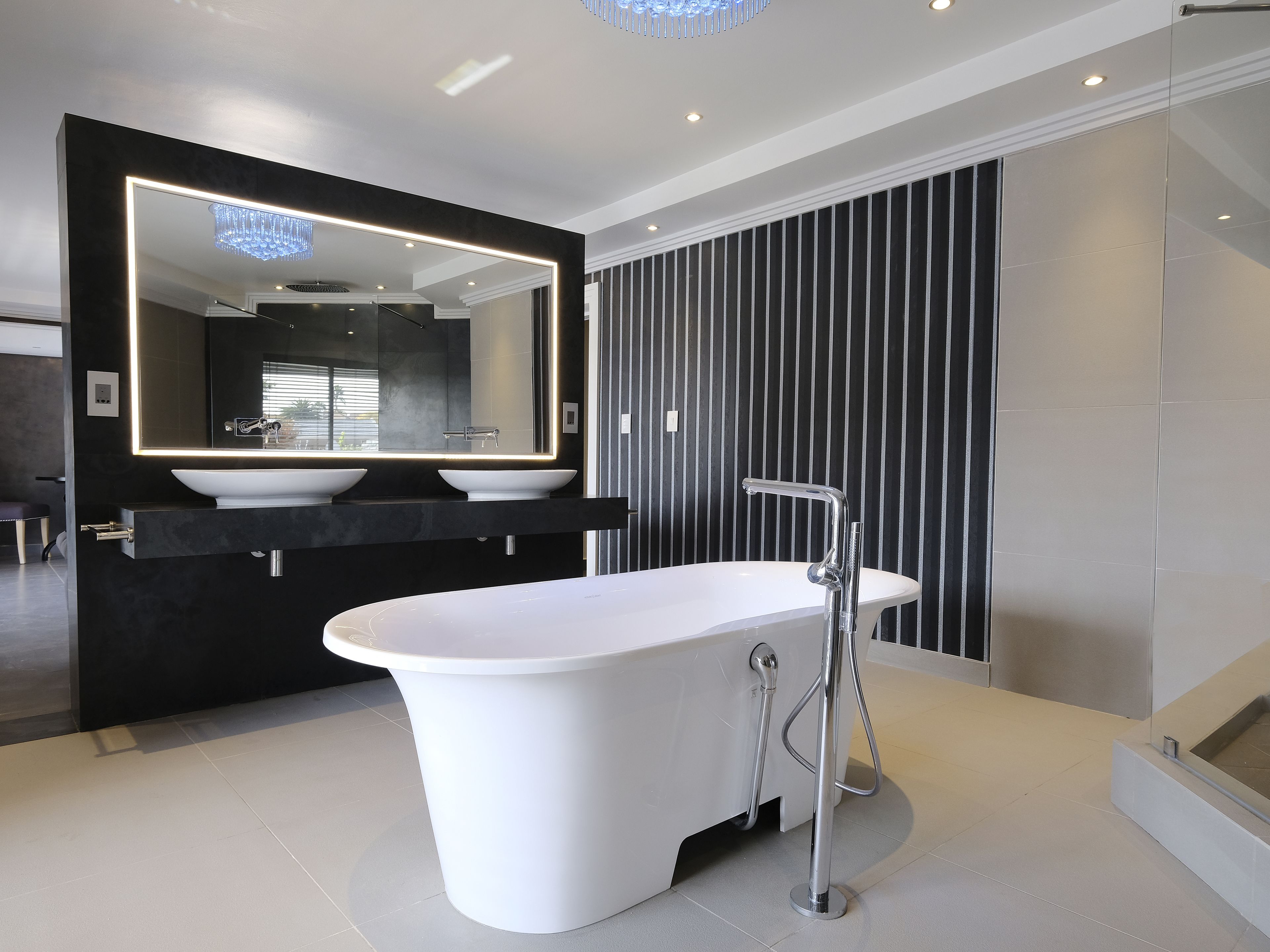 A modern bathroom with a freestanding bathtub, a large mirror, and a black vanity with two sinks.
