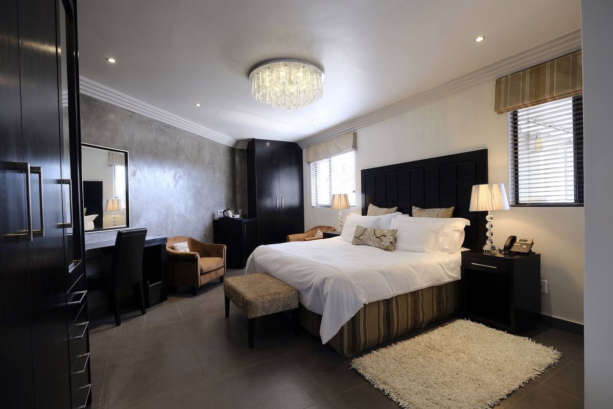 Une chambre à coucher moderne avec un grand lit, un bureau, une chaise, une coiffeuse et un lustre.