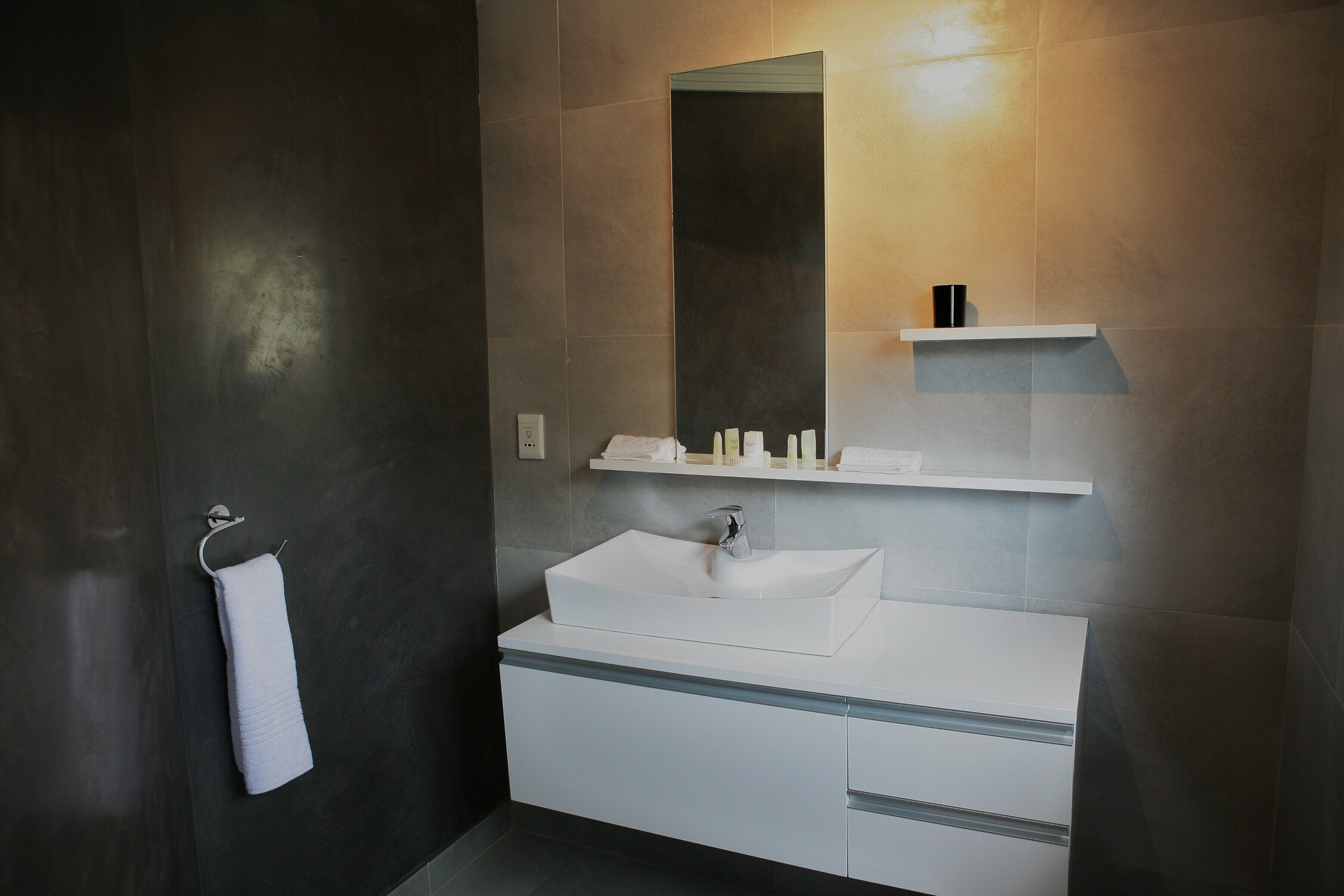 A modern bathroom with a large mirror, a white sink, and a towel rack.