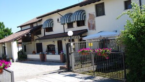 A two-story building with a tiled roof, a gated entrance, and a small patio area with potted plants and flowers. - Da Carla Trattoria con Locanda (Gambolo)
