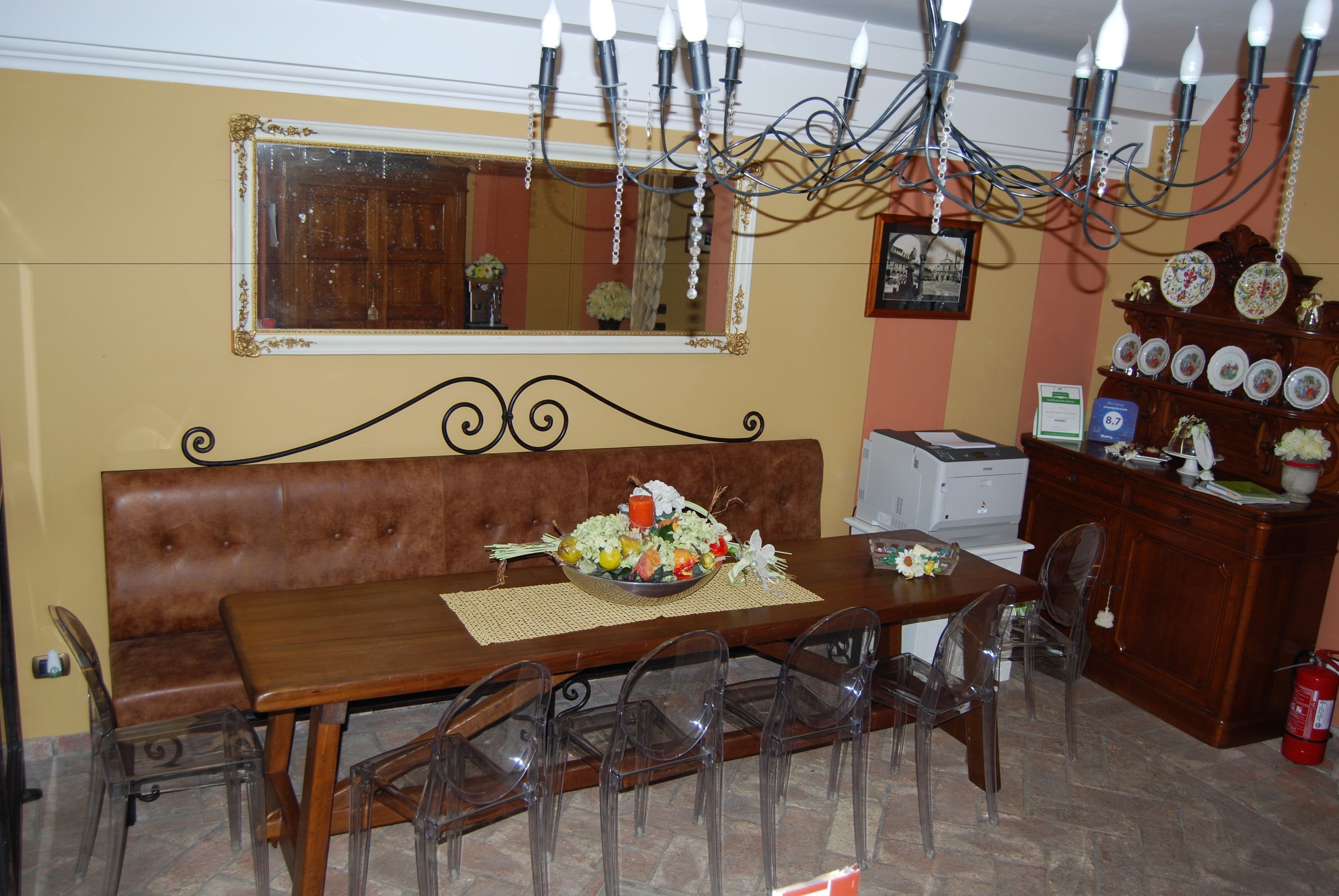 Un coin repas comprenant une table en bois, des chaises en plastique transparent, un banc en cuir marron, un lustre, un miroir et un porte-assiettes.