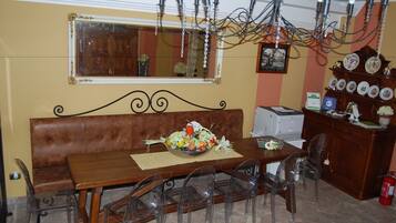 Un coin repas comprenant une table en bois, des chaises en plastique transparent, un banc en cuir marron, un lustre, un miroir et un porte-assiettes.