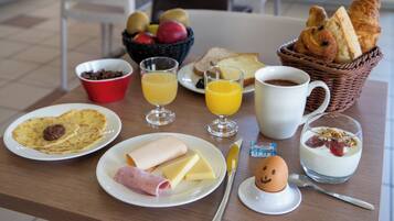 A breakfast table with plates of food, a basket of bread, a bowl of fruit, and a cup of coffee.