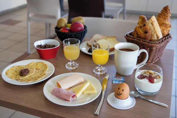 Une table de petit-déjeuner avec des assiettes remplies de nourriture, un panier de pain, un saladier de fruits et une tasse de café.