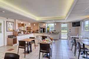 Una cafetería moderna con una barra central, zona de estar y un televisor en la pared.