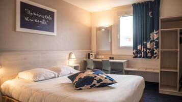 A hotel room with a bed, a desk, a chair, a wardrobe, and a window with curtains.
