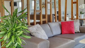 A modern living room with a grey sofa, a red pillow, and a green plant. - Ace Hotel Clermont-Ferrand La Pardieu (Clermont-Ferrand)