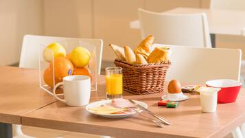 A breakfast table with a basket of bread, a mug, a plate with eggs, and a glass of orange juice.