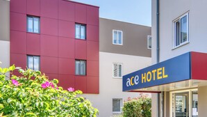 A modern hotel with a red and beige facade, a visible entrance, and a signboard. - Ace Hotel Clermont-Ferrand La Pardieu (Clermont-Ferrand)