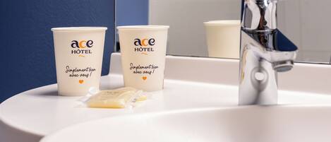 Dos tazas blancas con la marca 'ace HOTEL' y un grifo plateado sobre un lavabo blanco.