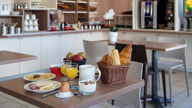 A breakfast setup with plates of food, a basket of bread, and a coffee machine. - Ace Hotel Clermont-Ferrand La Pardieu (Clermont-Ferrand)