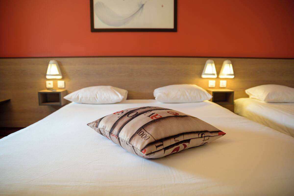 Een hotelkamer met twee bedden, elk voorzien van witte beddengoed en kussens, en twee bedlampen.
